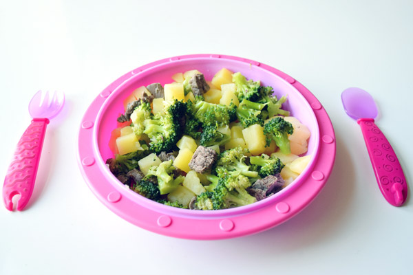 Babybrei Zutaten Kartoffeln, Fleischstücke und Brokkoli auf einem Kinderteller mit Kinderbesteck