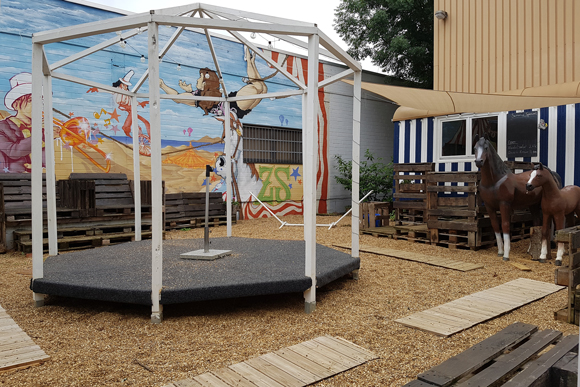 Vor dem Eingang zur ZIRKUSfabrik in Köln Dellbrück, Foto: Silke Büscher Eingangsbereich Zirkusfabrik mit Zirkusbild, kleiner Bühne und Plastik-Pferden